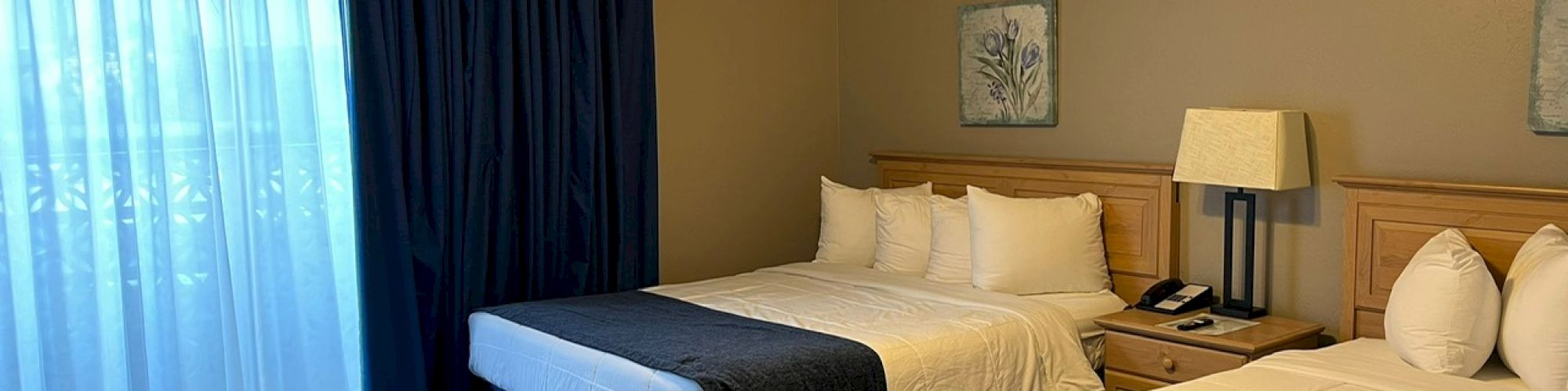 This image shows a hotel room with two beds, a ceiling fan, bedside table, lamp, and a phone, with sliding glass doors covered by curtains.