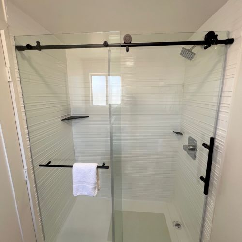 A modern shower with glass sliding doors, a towel rack with a white towel, and a rain showerhead are visible.