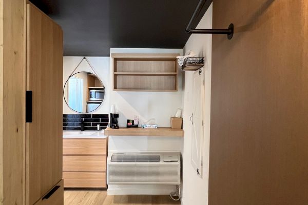 Room with wooden floors, a closet, wall shelf, and vanity with a round mirror. An HVAC unit is beneath a small counter.