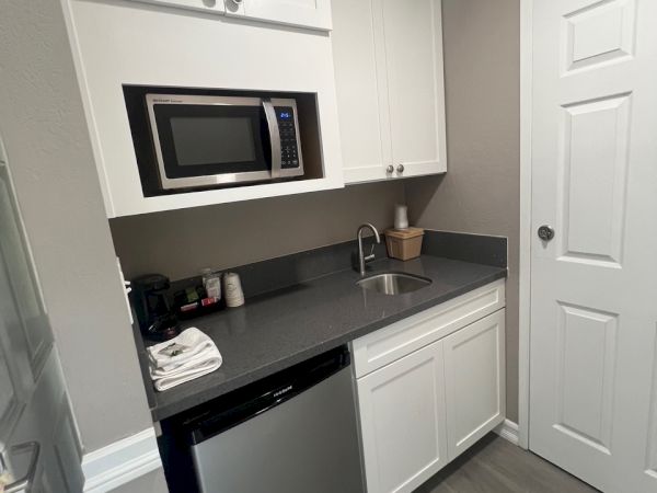 A compact kitchen with a microwave, sink, cabinet, fridge, and countertop, featuring a minimalist and modern design.