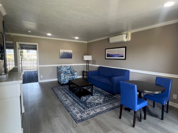 A modern living room with a blue sofa, matching chairs, a rug, and wall art, featuring wood flooring and neutral walls.