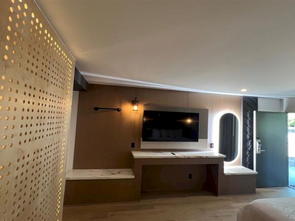 The image shows a modern room with a TV, wooden accents, a lit-up perforated partition, and a door leading outside.