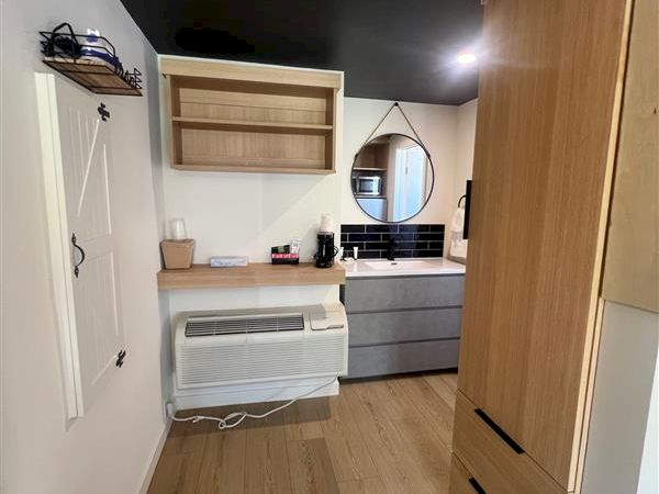 A modern room with wooden furniture, shelves, a dresser, circular mirror, and light wood flooring, giving a cozy and organized feel.