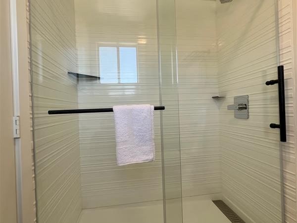A modern shower with glass doors and black hardware, featuring a towel hanging inside and white tiled walls, with a rainfall showerhead.